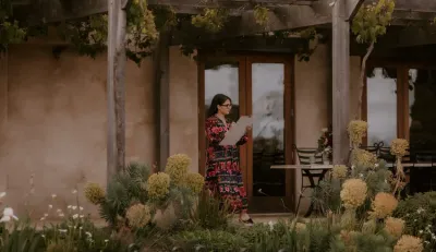 Artist Alyssa Bermudez sketching on a drawing board under a vine-covered pergola at a wedding, by Alyssa Bermudez Art