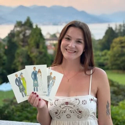Artist Charlotte Beddoes holding three watercolour wedding guest illustrations by a lake view, by Charlotte Beddoes