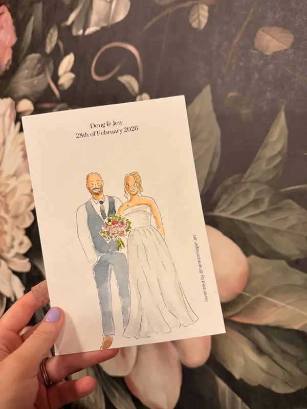 Ink and watercolour illustration of a bride and groom on a personalised card held up to floral wallpaper, by Hannah Megan Art