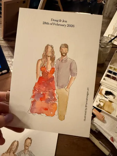 Ink and watercolour portrait of a wedding guest couple on a personalised card beside a paint palette, by Hannah Megan Art